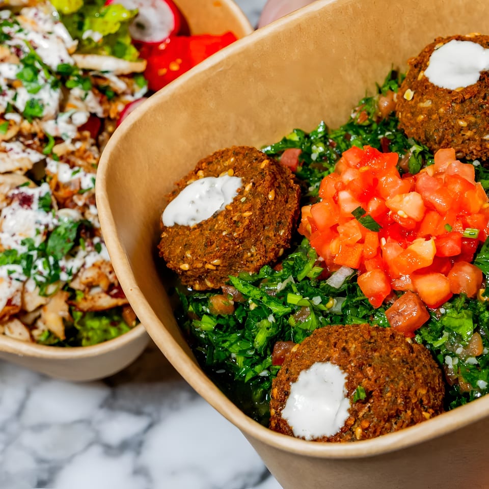 Two bowls of Middle Eastern food, one with falafel and tabbouleh, the other with chicken and salad.