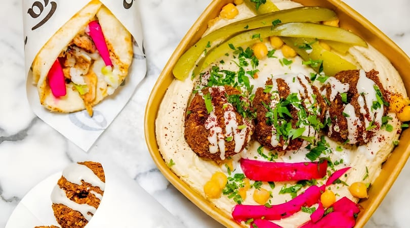 A falafel plate with hummus, pickles, and a chicken shawarma wrap on a marble surface.