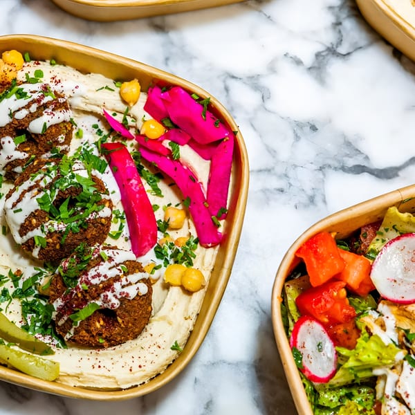 Falafel with hummus, pickled turnips, and a side salad in eco-friendly containers on marble.