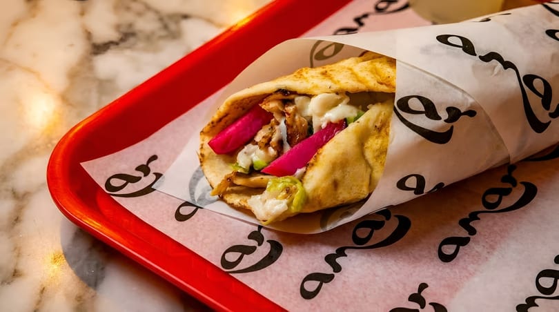 A chicken shawarma wrap with pink pickled turnips and white sauce, on a red tray.