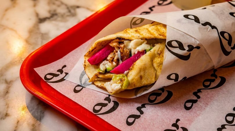 Chicken shawarma wrap with pickled turnips and garlic sauce, served on a red tray.