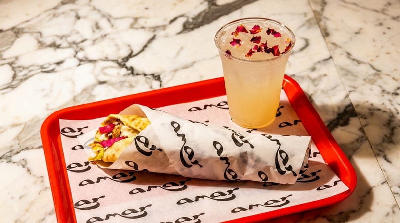 A chicken shawarma wrap and a drink with rose petals on a red tray.