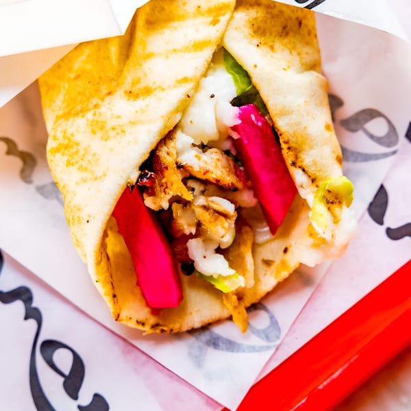 A close-up of a chicken shawarma wrap with bright pink pickled turnips and white sauce.