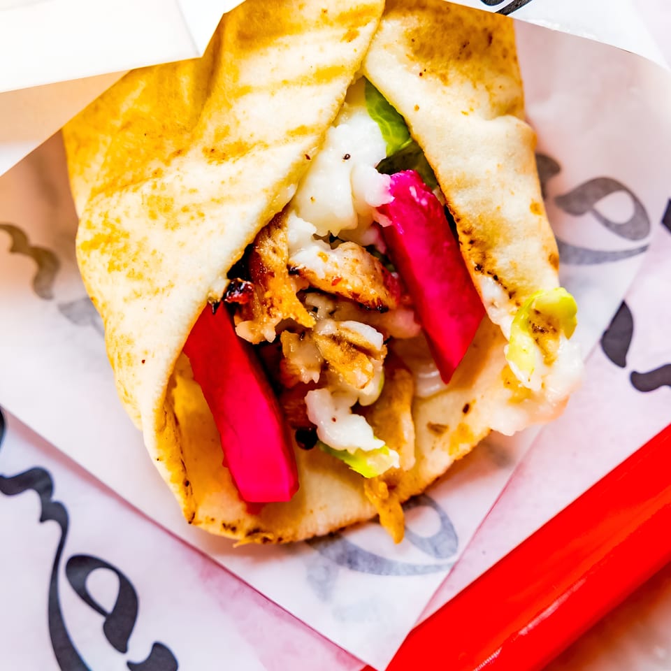 A close-up of a chicken shawarma wrap with bright pink pickled turnips and white sauce.